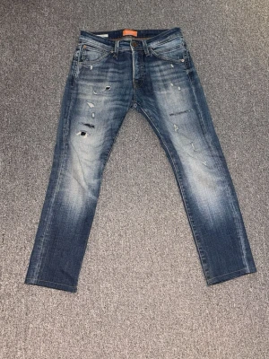 Blå slitna jeans från Jack & Jones - Ljusblå jeans från Jack & Jones i storlek W29 med klassiska slitningar i nyskick. Jeansen är knappt använda och har inga deffekter. Perfekt för sommaren!