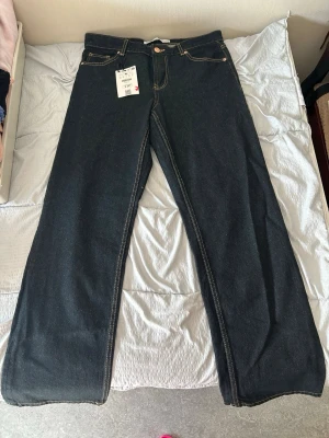 Mörkblå raka jeans med kontrastsömmar - Nya oanvända snygga mörkblå jeans med raka ben och kontrastsömmar. Klassisk femficksmodell och hög midja. Jeansen har en enkel knappstängning och är tillverkade i kraftig denim. Perfekta för en clean och tidlös look.