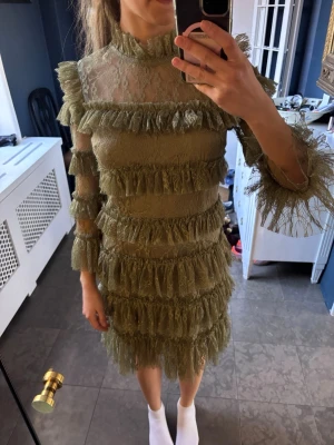 By Malina klänning - Aldrig använd, prislapp kvar. Klänningen har långärmade ärmar med transparent spets och flera lager volangdetaljer över hela plagget. 