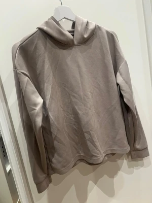 Beige hoodie i mjukt material - En stilren beige hoodie med huva och långa ärmar. Tillverkad i ett mjukt, fleeceliknande material som känns skönt mot huden. Hoodien har en avslappnad passform och ribbade muddar vid ärmsluten. Perfekt för en chill och enkel look.