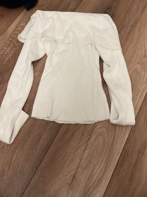 Vit offshoulder topp från BikBok - Säljer en vit ribbad offshoulder topp från BikBok i storlek S. Toppen har långa ärmar och en snygg volangkant över axlarna. Perfekt för dig som gillar stilrena och trendiga plagg med en feminin touch.