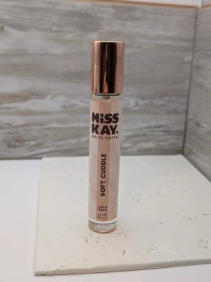 Miss Kay Soft Cuddle parfym 25 ml nästan full - Miss Kay Soft Cuddle Eau de Parfum i en smal glasflaska med roséguldfärgat lock. Doften är tillverkad i Italien och flaskan har en stilren design med ljusrosa etikett och tydlig text. Perfekt att ha med i väskan för en fräsch känsla hela dagen.