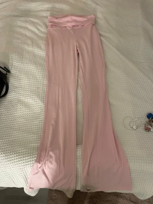 Ljusrosa utsvängda yoga pants Gina Tricot - Säljer ett par ljusrosa yoga pants från Gina Tricot i storlek XS. De har hög midja och utsvängda ben, vilket ger en snygg retrovibe. Mjukt och stretchigt material som sitter bekvämt. Perfekta för dig som gillar en trendig och avslappnad stil.