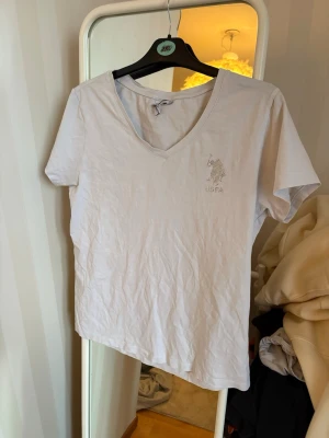 Vit v-ringad t-shirt från U.S. Polo Assn - Klassisk vit t-shirt från U.S. Polo Assn med v-ringning och  logga broderad på bröstet 💯. Tillverkad i mjuk bomull och har korta ärmar för en enkel och clean look. Jättefin och jätteskön på. 🤍