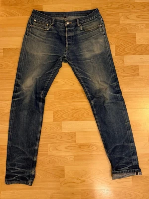 Apc petite new standard - Snygga mörkblå selvedge jeans med feta slitningar. Jeansen är från början w33, men är omsydda i midjan för att passa w31. Det är ett hål i höger framficka, men har utöver det mycket liv kvar i sig! Hör av dig vid eventuella frågor.