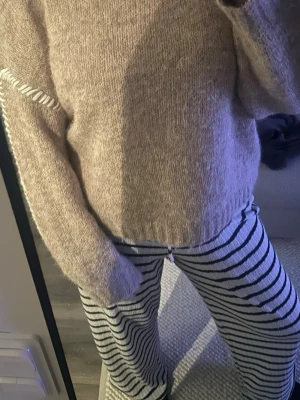 Beige stickad tröja från JDY - Mysig beige stickad tröja från JDY med rund halsringning och diskret vit detalj längs axlarna. Tröjan har en avslappnad passform och ribbstickade muddar vid ärmslut och nederkant.🤎