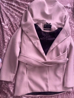 Ljusbeige kappa från Amisu - Stilren ljusbeige kappa från Amisu Classic Collection med knytskärp i midjan och stora slag. Kappan har dubbelknäppning framtill och svart innerfoder. Perfekt för dig som vill ha en klassisk och elegant look.