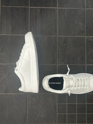 Vita sneakers från Björn Borg - Stilrena helvita sneakers från Björn Borg med klassisk låg profil. Skorna har vita snören, diskret logga på plösen och ovandel i slätt syntetmaterial. Perfekta för en clean och fräsch look till alla outfits. Använd en gång, pris kan diskuteras
