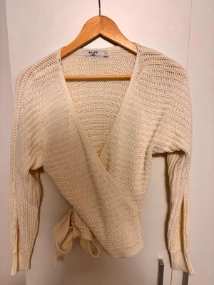 Vit omlottstickad tröja NA-KD - Säljer en vit stickad omlottopp från NA-KD med långa ärmar och knytband i midjan. Tröjan har en djup V-ringning och är gjord i ett mjukt, grovstickat material som ger en avslappnad men trendig look.