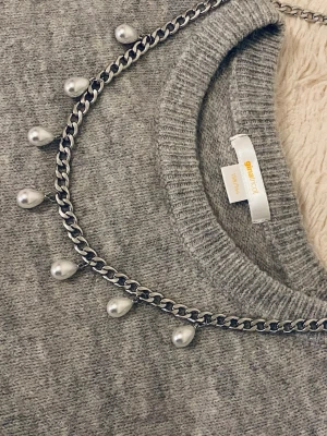 Kedjehalsband med droppformade pärlor - Snyggt halsband med en silverfärgad kedja och droppformade vita pärlor som hänger längs hela kedjan. Perfekt accessoar för att lyfta vilken outfit som helst med en trendig och elegant touch. Passar dig som gillar statement-smycken och vill sticka ut.