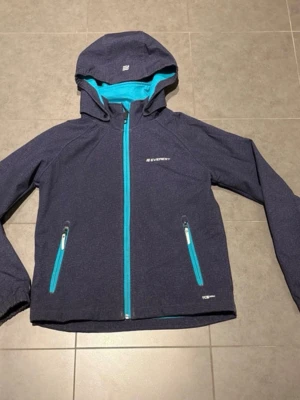 Mörkblå vindjacka från Everest - Snygg mörkblå vindjacka från Everest med turkosa detaljer, dragkedjor och innerfoder. Jackan har huva, två fickor med dragkedja och är tillverkad i ett lätt och smidigt material som passar perfekt för blåsiga dagar. Vid ena armen hsr jackan blivit lite nöt men annars i fint skick. Se bilder