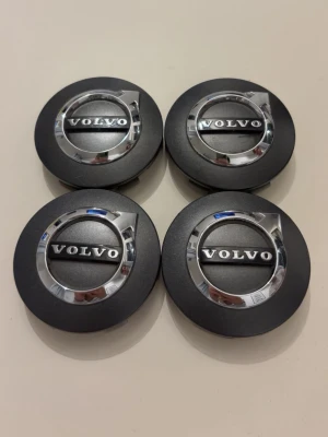 Volvo centrumkåpor 4-pack svart silver - Fyra stycken runda centrumkåpor till Volvo i svart och silver med klassisk Volvo-logga i mitten. Tillverkade i plast och metall, passar perfekt till bilens fälgar för en snygg och stilren look.