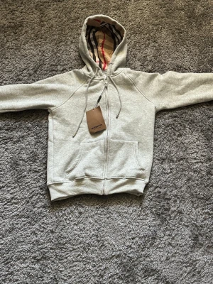 Burberry grå zip up hoodie - Burberry hoodie säljes. Iväldigt fint skick, inga fläckar eller skador.   Storlek: XS men S funkar Pris: 400   Frakt betalas av köparen eller möts upp i Östersund 
