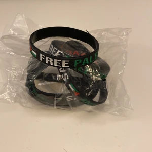 Svart Free Palestine armband  - Svart armband i silikon med texten 'FREE PALESTINE' och 'SAVE GAZA' i vitt, rött och grönt. Armbandet har även en liten flaggdetalj i samma färger. Perfekt accessoar för att visa stöd och engagemang. 