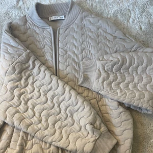 Beige jacka från Monki - Säljer en beige/grönish superskön vårjacka från Monki med vågigt mönster. Jackan har dragkedja framtill, ribbade muddar vid ärmslut samt två fickor. Jätteskönt material och supersnygg. Säljer för att den ej kommer till användning, men det är så snygg 🩷🩷🩷 