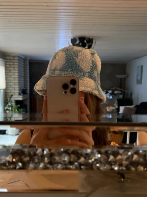 Blåvit teddy bucket hat  - Säljer en supermjuk och fluffig bucket hat i teddy-material. Hatten är ljusblå med stora vita hjärtan och har en avslappnad, bred brätte. Perfekt accessoar för att sticka ut och hålla sig varm. Passar dig som gillar gulliga och trendiga detaljer.