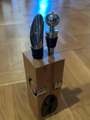 Vinset i trä med korkskruv och hällpip - Snyggt vinset med korkskruv, hällpip och flaskpropp i rostfritt stål och svart silikon. Allt levereras i ett stilrent ställ av trä som håller tillbehören på plats. Perfekt för vinälskare som vill ha allt samlat.