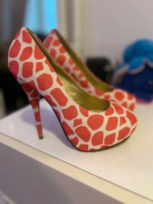 Rosa och vita pumps med mönster - Unika pumps med höga klackar i ett lekfullt rosa och vitt mönster. Skorna har rundad tå och är tillverkade i textilmaterial. Perfekta för dig som vill sticka ut och addera färg till din outfit.