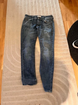 Blå jeans från Jack & Jones - Snygga vintage Jack N Jones byxor. Storlek 28/30. Fräsh slitning på benet och en unik design med en ficka som är röd och en som är vit. Vid fler frågor så är det bara att kontakta//Wille