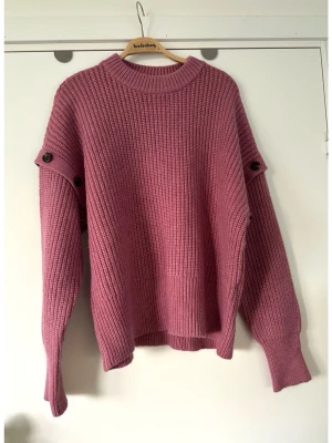 Co’Couture - Rosa stickad tröja med knappar - storlek M - Trendig rosa / lila stickad tröja från Co’Couture i storlek M med oversized passform och ribbstickad struktur. Tröjan har rund halsringning och dekorativa brunsvarta knappar längs ärmarna. Mjukt och halvfluffigt härligt material. Mycket gott skick, som ny!