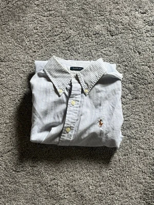 Randig skjorta från Ralph Lauren - Klassisk ljusblå och vit randig skjorta från Ralph Lauren med broderad logga på bröstet. Storlek small mycket bra skick!