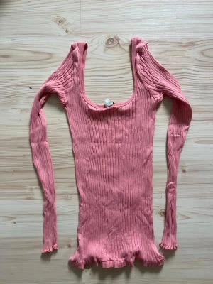 Rosa ribbad topp från Intimissimi - Supersnygg rosa långärmad topp från Intimissimi. Modellen är ribbad med en djup rundringning och har en croppad känsla med vågig kant nertill. Perfekt för dig som gillar en slim och figurnära passform. Den är oanvänd av mig men köpt på Vinted. 