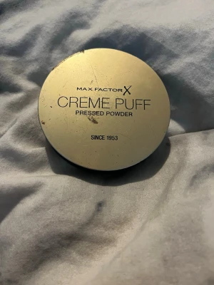 Max Factor Creme Puff Pressed Powder - Max Factor Creme Puff Pressed Powder i färgen 13 Nouveau Beige. Kompakt puder i rund brunfärgad dosa med svart botten. Ger en matt finish och jämnar ut hudtonen. Innehåller 14g och har en klassisk doft. Perfekt för att fixera foundation eller användas ensam.