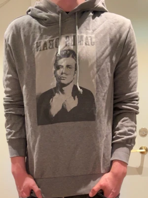 Unik Dolce & Gabbana hoodie - Snygg grå hoodie från Dolce & Gabbana med tryck av James Dean på bröstet. Hoodien har dragsko i huvan och ribbade muddar vid ärmar och nederkant. Tillverkad i mjukt material som känns skönt mot huden. Perfekt för en avslappnad och cool stil.