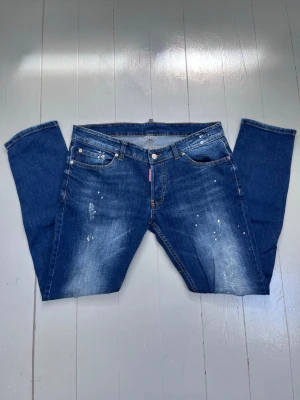 dsquared2 jeans - Säljer ett par blå jeans från dsquared2 med snygga slitningar, ljusa partier och vita färgstänk på framsidan. Pris kan diskuteras Italiensk storlek 44 (Motsvarar ca W30/L32) 