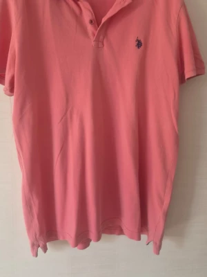 Rosa pikétröja från U.S. Polo Assn - Säljer en klassisk rosa pikétröja från U.S. Polo Assn med korta ärmar och liten broderad logga på bröstet. Tröjan har krage och knappar vid halsen, perfekt för en avslappnad men ändå stilren look.