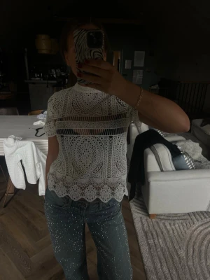 Vit spetsblus med kort ärm - Säljer en superfin vit blus i spets med korta ärmar och högt rundat halsringning. Blusen har ett detaljerat broderat mönster och är genombruten vilket ger en luftig och trendig look. Perfekt att styla med ett linne under eller som den är för en edgy vibe.