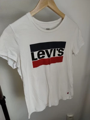 Två vita Levi's t-shirts med tryck - Säljer två vita t-shirts från Levi's med klassiska tryck framtill. Den ena har stort Levi's-logotyp i svart, blått och rött, den andra har 'Los Angeles Levi's' i svart och rött. Båda har rund hals och korta ärmar. Perfekta för en avslappnad streetstil.