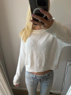 Vit croppad stickad tröja - Storlek 146/152. Säljer en vit croppad stickad tröja med rund hals och långa ärmar. Tröjan har en ribbad struktur och en relaxed, lite loose passform som passar perfekt till jeans eller kjol.