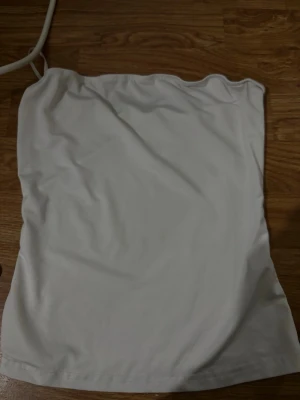Vit axelbandslös tubtopp - Säljer en enkel och stilren vit tubtopp utan axelband. Toppen har en rak passform och är perfekt att matcha med jeans eller kjol. Materialet känns mjukt och stretchigt, vilket gör den bekväm att bära hela dagen.