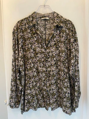 Blommig långärmad blus från Only - Snygg blus från Only med grönt, rosa och vitt blommönster. Blusen har krage, knappar framtill och långa ärmar med lös passform. Perfekt för dig som gillar en avslappnad men trendig stil. Materialet känns mjukt och följsamt.