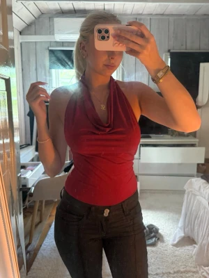 Vinröd halterneck body - Säljer en vinröd halterneck body med draperad urringning. Toppen är tight och ärmlös, perfekt för dig som vill ha en stilren och trendig look. Materialet känns mjukt och stretchigt, troligen polyester eller bomullsmix.