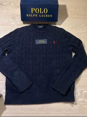 Mörkblå kabelstickad tröja Polo Ralph Lauren - Säljer polo Ralph Lauren kabel stickad tröja men tyvärr har den lite fläckar och 2 små hål.tillbehlr ingår inte.😊😊