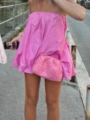 Rosa kort klänning med ballongform - En superfin rosa kort klänning med ballongformad nederkant och axelbandslös design. Perfekt för dig som vill ha en lekfull och trendig look. Klänningen är gjord i ett lätt bomullsmaterial som känns skönt mot huden och passar perfekt till varma dagar.