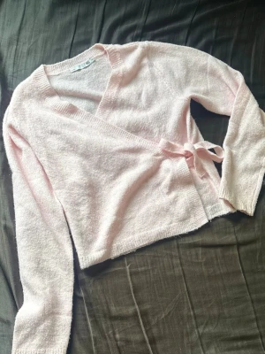 Ljusrosa omlottkofta - Supersöt ljusrosa omlottkofta med knytband i midjan. Koftan har lång ärm och är stickad i ett mjukt, fluffigt material som känns riktigt mysigt. Den är i stl 150 då min storlek var slut och denna passade på mig som brukar ha S. Använd en gång