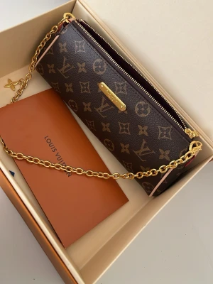 Kuvertväska med mönster - Snygg kuvertväska.Väskan har guldfärgad kedja, dragkedja upptill och detaljer i läder. Perfekt accessoar för dig som vill ha något lyxigt och tidlöst.