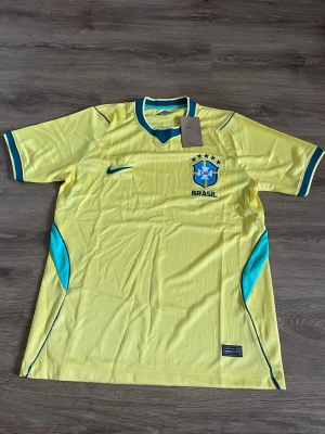 Gul Brasil Nike fotbollströja - Säljer en gul Brasilien fotbollströja från Nike med blå detaljer och gröna inslag. Tröjan har korta ärmar, rund hals och Brasil-logga med fem stjärnor på bröstet. Tillverkad i lätt och ventilerande material, perfekt för träning eller match.