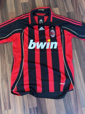 AC Milan hemma tröja 2007 ( Kaka ) - Säljer en klassisk AC Milan matchtröja från Adidas med röda och svarta vertikala ränder, klubbmärke på bröstet och Bwin som sponsortryck. Tröjan har korta ärmar, krage och gula detaljer. Perfekt för fotbollsfans! Speciellt Kaka fans💯