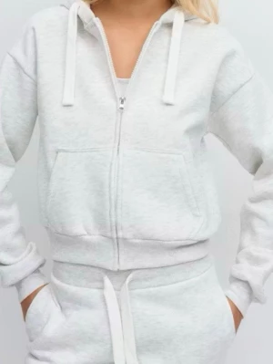 Ljusgrå zip hoodie med huva - Säljer en ljusgrå hoodie med dragkedja, huva med vita snören och två stora fickor framtill. Hoodien har ribbade muddar vid ärmslut och nederkant. Perfekt för en chill och avslappnad stil. Materialet är mjukt och skönt, troligen bomullsblandning.