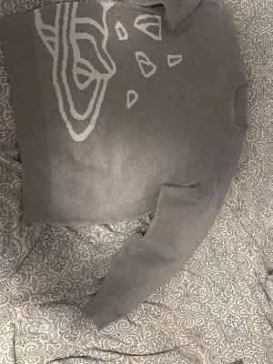 Grå stickad tröja med rymdmotiv - Snygg grå stickad tröja med vita grafiska rymdmotiv som planeter och stjärnor på både fram- och baksidan. Tröjan har rund halsringning och ribbade muddar vid ärmslut och nederkant. Perfekt för dig som gillar unika prints och en chill stil.