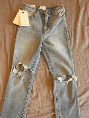 Ljusblå ripped jeans från Asos - Säljer ett par ljusblå jeans från Asos med hög midja och raka ben. Jeansen har stora slitningar vid knäna för en trendig, avslappnad look. Klassisk femficksmodell och tillverkade i bomull. Perfekta för dig som gillar streetstyle.