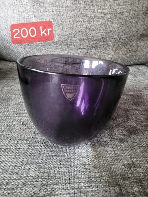 Lila glaskål från Orrefors - Säljer en snygg lila glaskål från Orrefors. Skålen har en rund form och är tillverkad i tjockt glas med en djup lila ton. Perfekt som dekoration eller för att servera snacks. Orrefors-loggan sitter kvar på skålen.