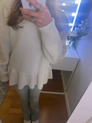 Vit stickad volangtröja - Supersöt vit stickad tröja med volangkant nertill och ribbad struktur. Tröjan har långa ärmar och en avslappnad passform, perfekt att styla med jeans eller kjol. Materialet känns mjukt och bekvämt mot huden. Knappt använd💓 Storlek S men är ganska liten så passar Xs också🫶🏻🫶🏻