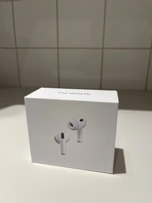 Apple AirPods Pro trådlösa hörlurar - Säljer ett par vita Apple AirPods Pro med stilren design och silikonpluggar för bästa passform. Hörlurarna är trådlösa in-ear och levereras i originalförpackning. Perfekta för dig som vill ha grymt ljud och smidig anslutning till din iPhone eller andra Apple-enheter.