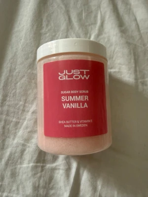 Just Glow Summer Vanilla Body Scrub - Oöppnad och plomberad. Sockerbaserad body scrub från Just Glow med doft av summer vanilla. Innehåller sheasmör och vitamin E för extra återfuktning. Kommer i en genomskinlig plastburk med vit skruvlock och rosa etikett. Tillverkad i Sverige. Nypris 399kr