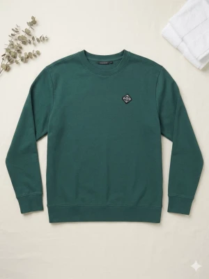 J.Lindberg Mörkgrön crewneck sweatshirt - Mörkgrön sweatshirt från Cotton On med rund halsringning och liten svartvit patch på bröstet. Tröjan har ribbade muddar vid ärmslut och nederkant. Tillverkad i mjuk bomullsblandning, perfekt för en avslappnad stil.